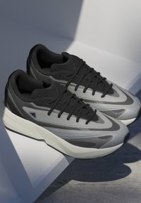 Sive i crne atletske cipele sa elegantnim dizajnom, koje koriste teksturirane materijale, istaknute vezice i bijelu Lightstrike đon.