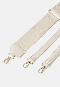 Beige verstelbare strap van stof met leren accenten, voorzien van goudkleurige metalen clips en een subtiel bloemmotief.