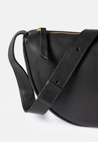 Black leather crossbody bag with adjustable strap, gold zipper, and leather zipper pull on a white background.