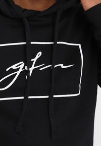 Felpa nera con logo bianco in un contorno rettangolare. Presenta un cappuccio e lacci per la regolazione, realizzata in un morbido materiale misto cotone.