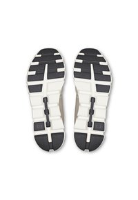 Shoe soles with a beige and black color scheme. Featuring cloud-like cushioning, a segmented design, and textured grip patterns.