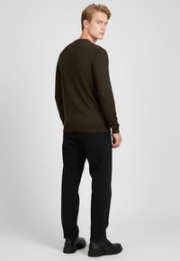 Tmavě zelený svetr s dlouhými rukávy a kulatým výstřihem, texturovaná látka a žebrované manžety, kombinovaný s černými džínami a černými botami.