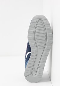 Chaussure de sport pour homme en suède bleu marine avec des accents blancs et bleus. Elle dispose d'une semelle en caoutchouc gris texturé avec un motif strié pour une meilleure adhérence.