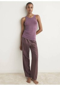 Lila, figursydd linne topp tillsammans med vida, löst sittande bruna byxor. Slät tygtextur. Stående modell på en neutral bakgrund.