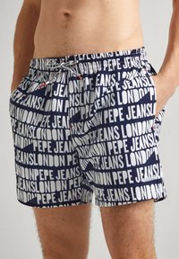 Mornarske kupaće gaće tamnoplave boje s ponavljajućim uzorkom "PEPE JEANS LONDON" u bijeloj boji. Elastična stražnja traka s vezicom. Ima bočne džepove i meku teksturu.
