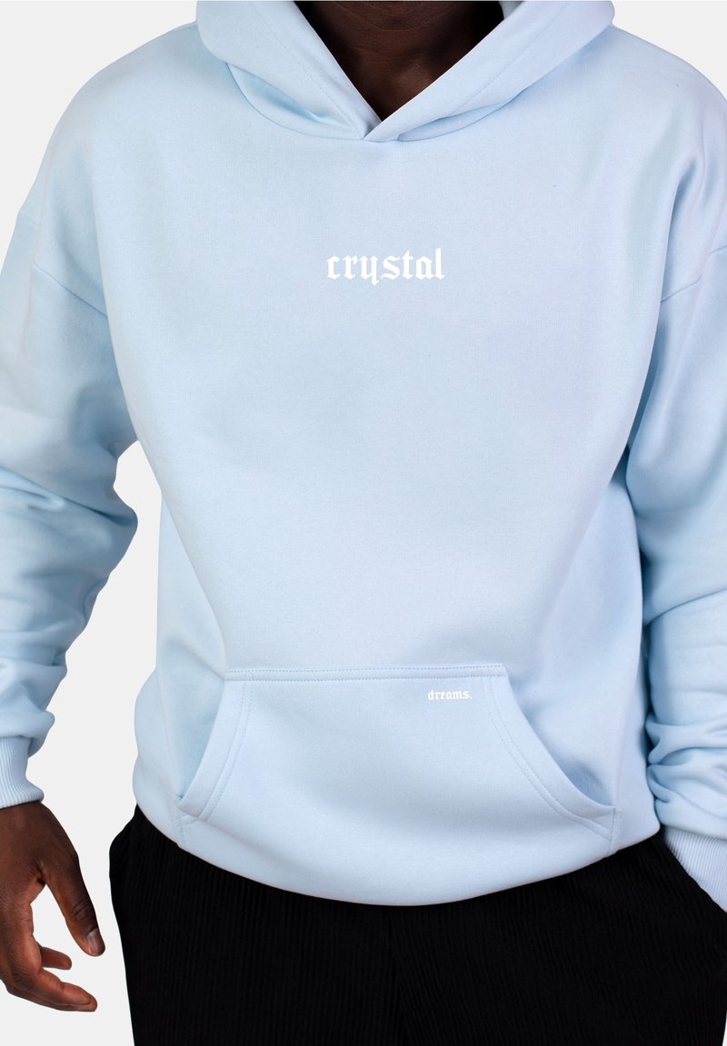 Ljusblå hoodie tillverkad av mjukt tyg, med en framsida ficka och vit text "crystal" och "dreams." på bröstet och fickan.