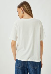 Hvid bomulds-tshirt med korte ærmer, der har en afslappet pasform og en rund halsudskæring, parret med blå denimbukser.