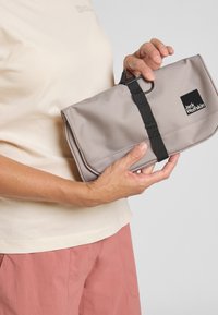 Grijze stoffen toilettas met zwarte band en clip, voorzien van het Jack Wolfskin-logo. Opgevouwen ontwerp, gladde textuur en rechthoekige vorm.