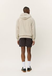 Cream hoodie with logo on back, black shorts with subtle pattern, white socks, and black shoes. Smooth texture, relaxed fit.