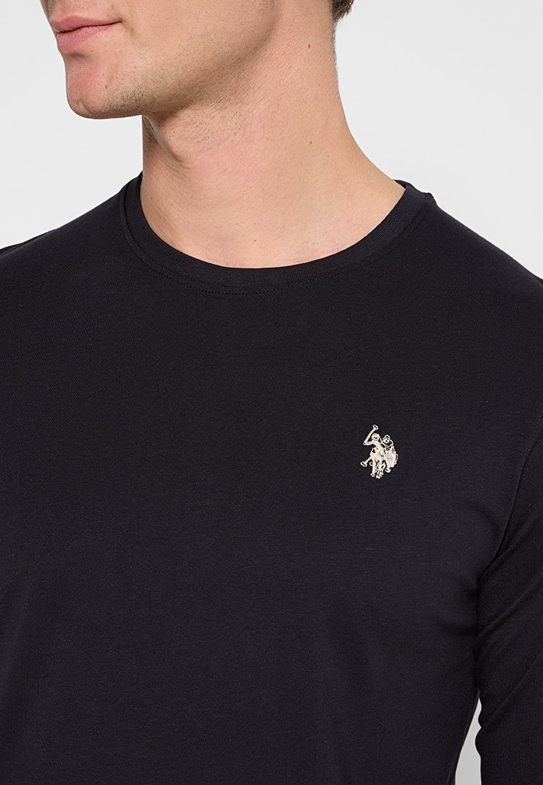 T-shirt noir à manches longues en tissu doux, avec un col rond et un petit logo brodé sur la poitrine.