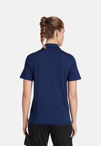 Marineblaues Polohemd aus atmungsaktivem Material, mit klassischem Kragen und kurzen Ärmeln. Die Rückansicht hebt die glatte Textur und die taillierte Passform hervor.