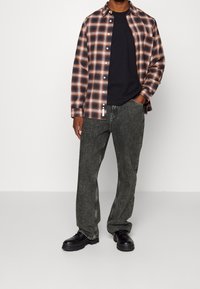 Black short-sleeve t-shirt under a brown and orange plaid shirt, paired with dark gray wide-leg pants and black lace-up shoes.