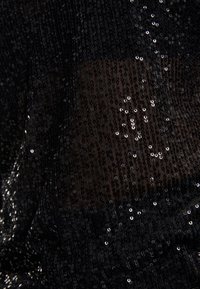 Tissu noir recouvert de petits sequins noirs densément emballés, certains réfléchissant la lumière, montrant un motif texturé subtil.
