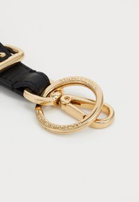 Cintura in pelle nera con hardware in metallo dorato, dotata di un anello per chiavi circolare e dettagli incisi, che mettono in evidenza il nome del marchio e la città.