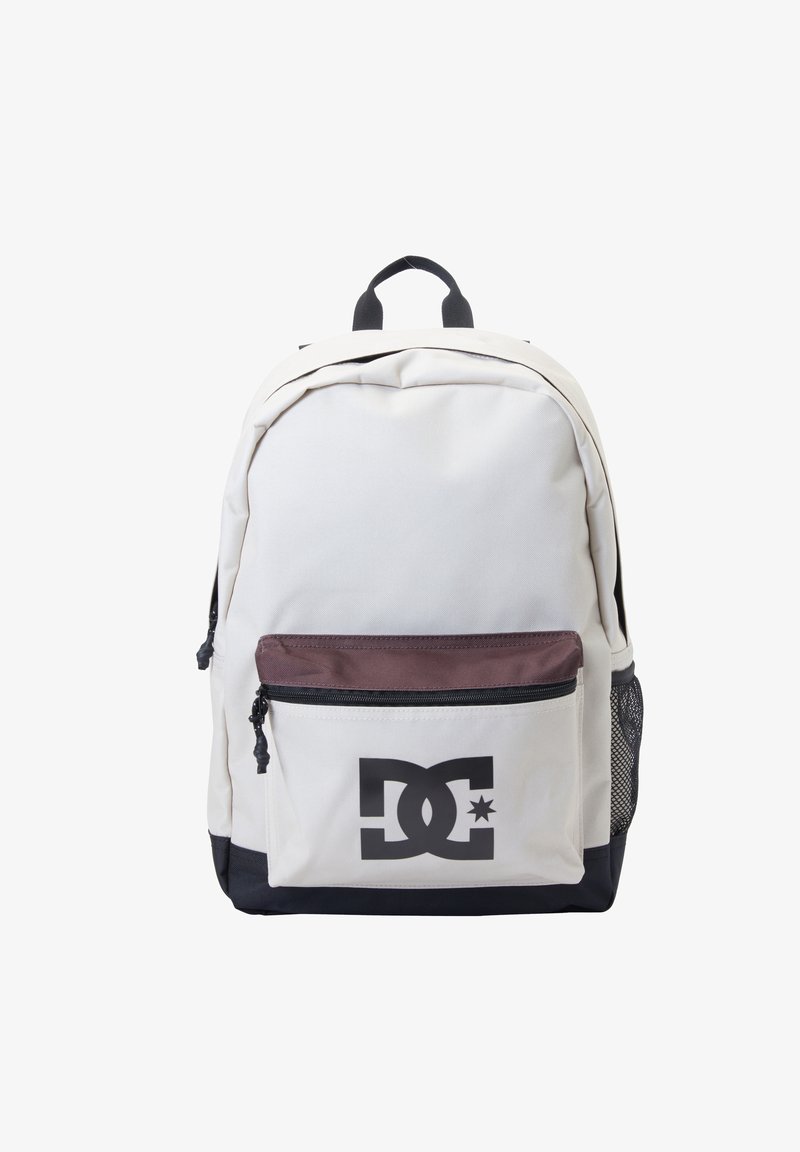 Sac à dos beige avec base noire, poche avant zippée marron, poche latérale en mesh noir et logo DC noir sur la poche avant.