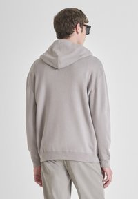 Sudadera gris claro con una textura suave, con capucha ajustable, corte relajado, puños y dobladillo acanalados. Combinada con pantalones beige.