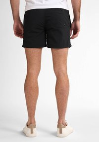 Shorts negri dintr-un material ușor, cu un design simplu, având un buzunar la spate și o margine curată. Purtați cu adidași bej.