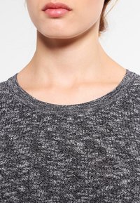 Pull en tricot gris avec un motif texturé et un col rond. Gros plan sur le col et le détail tissé du tissu, mettant en valeur différentes nuances.