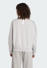 Sweatshirt oversize gris clair avec une taille et des poignets côtelés. Présente une étiquette verticale au niveau de la nuque à l'arrière. Texture de tissu doux.