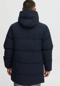 Chaqueta de plumón azul marino con capucha, que presenta secciones acolchadas horizontales, un ligero brillo y puños elásticos.