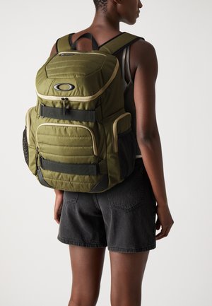 Sac à dos vert avec des accents noirs, doté d'un dos rembourré, de multiples poches, de bretelles réglables, de poches latérales en mesh et d'une fermeture éclair.