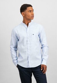 Camicia a maniche lunghe azzurro chiaro con colletto a band, patta dei bottoni frontale e tasca sul petto con un piccolo logo. Tessuto liscio, vestibilità sagomata.