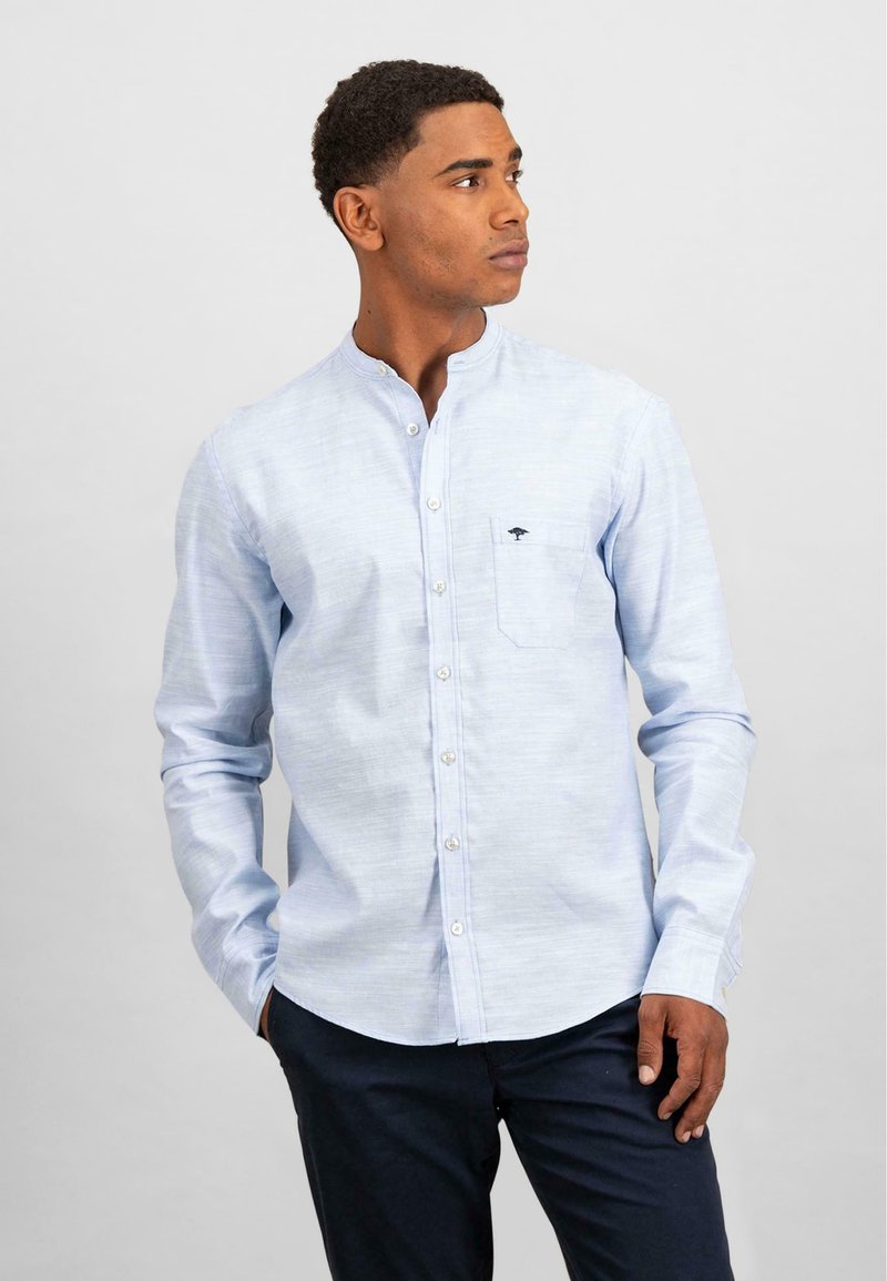 Camicia a maniche lunghe azzurro chiaro con colletto a band, patta dei bottoni frontale e tasca sul petto con un piccolo logo. Tessuto liscio, vestibilità sagomata.