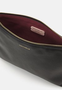 Bolsa de cuero negro con exterior texturizado. Interior forrado en tela burdeos, con una cremallera dorada y una etiqueta con la marca. Diseño sencillo.
