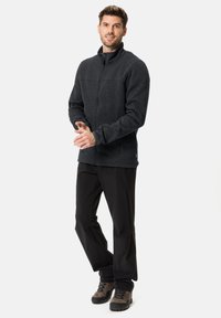 Veste en polaire gris foncé avec un col montant, une fermeture éclair à l'avant et deux poches latérales, associée à un pantalon noir et des bottes grises.