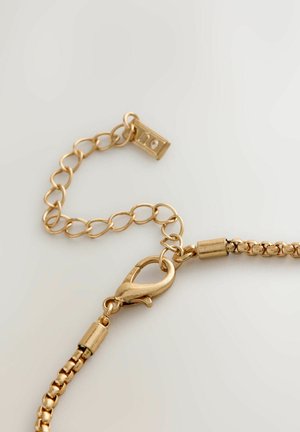 Goldene Kette mit einem strukturierten Gliederdesign, ausgestattet mit einem Karabinerverschluss und einem kleinen rechteckigen Hardwaredetail. Glatte Oberfläche, metallischer Glanz.