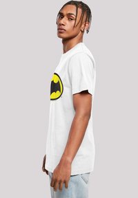 White cotton t-shirt featuring a large black and yellow Batman logo at the chest. Short sleeves and standard fit. Casual design.