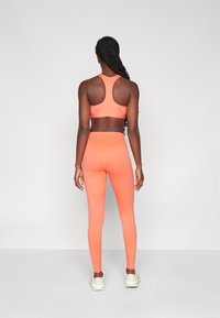 Lyse oransje sports-bh og tights laget av stretchy materiale, med racerback-design og en mid-rise midje med sømdetaljer.