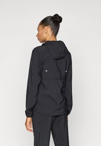 Veste noire avec capuche, dotée d'un panneau contrastant à l'arrière et d'accents réfléchissants. Fabriquée en matériau lisse et léger.