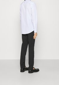 Maglietta button-up a righe blu chiaro con maniche lunghe, infilata in pantaloni scuri, abbinata a scarpe slip-on nere. Sfondo semplice.