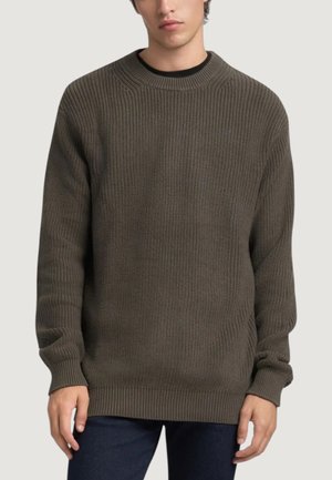 Dunkelgrüner, strukturiert gestrickter Pullover mit rundem Ausschnitt und gerippten Bündchen und Saum, getragen mit dunkelblauen Jeans.