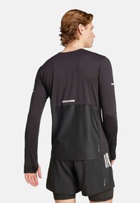 Zwarte lange mouw sporttop met een gestructureerd mesh onderpaneel, reflecterende details en een minimalistisch ontwerp. Gecombineerd met zwarte shorts.
