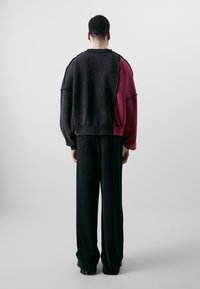 Schwarzes und burgunderfarbenes oversized Sweatshirt mit sichtbaren Nähten, Rundhalsausschnitt und lockerem Schnitt, kombiniert mit schwarzen weiten Hosen.