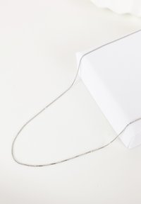 Collier en chaîne en argent avec une surface délicate et texturée ; maillons lisses et arrondis ; présenté sur une surface blanche à côté d'une boîte blanche.