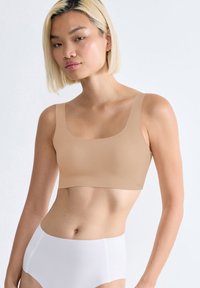 Beige geknipte bh met brede bandjes en een ronde halslijn, gemaakt van zachte stof. Draagt bij hoge taille witte onderbroek.