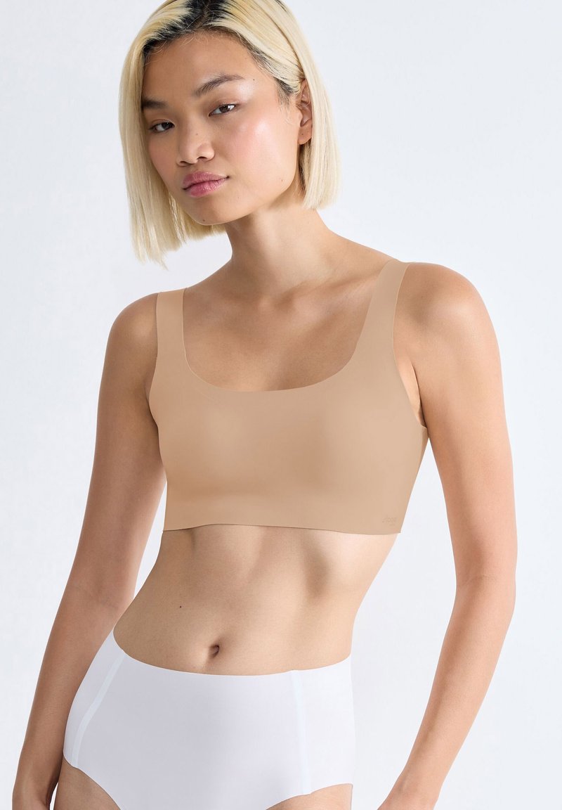 Beige geknipte bh met brede bandjes en een ronde halslijn, gemaakt van zachte stof. Draagt bij hoge taille witte onderbroek.