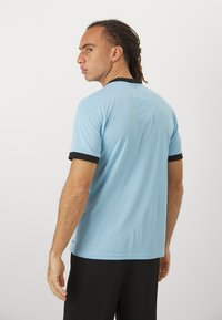 Lyseblå kortærmet skjorte med sort kant, der har en ribbet tekstur. Bagsiden viser et simpelt design med en lige kant. Sorte bukser.