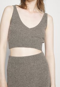 Top corto in maglia marrone con scollatura a V, bordi a costine e una finitura testurizzata. Abbinato a una gonna in maglia coordinata. Tessuto morbido e caldo.