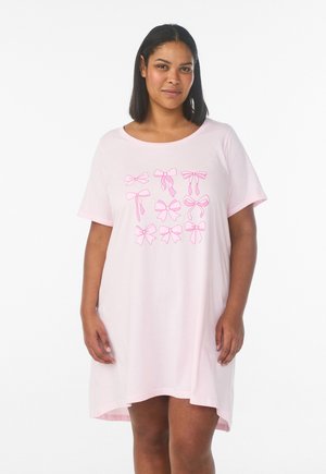 Žena v svetloružových šatách s krátkym rukávom, na prednej strane s deviatimi rôznymi ružovými ilustráciami mašlí, stojaca na bielom pozadí.