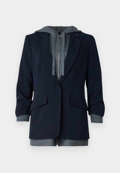 Tengerészkék blazer, szürke kapucnis belső résszel; cipzárral, két elülső zsebbel és bordázott mandzsettákkal a kiegészítő textúra érdekében.