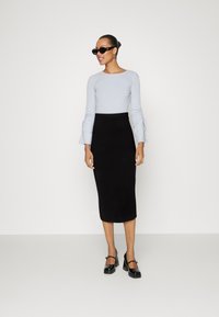 Light blue ribbed long-sleeve top with tie details at cuffs, paired with a black knee-length pencil skirt and black heeled shoes.