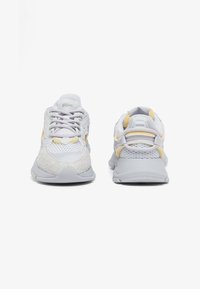 Sneakers grigio chiaro con accenti gialli, realizzati in materiali in rete e testurizzati, con colli imbottiti e suola in gomma. La vista frontale mostra il design con lacci.