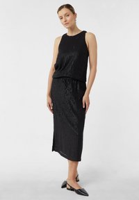 Czarna sukienka z pionowym wzorem w paski, bez rękawów, z rozcięciem. Wykonana z miękkiej tkaniny o delikatnym połysku. W zestawie z czarnymi, płaskimi butami.