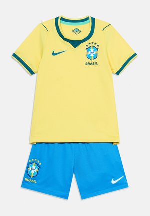 Κίτρινη φανέλα ποδοσφαίρου της Βραζιλίας με μπλε περιθώριο, έμβλημα της Βραζιλίας και λογότυπο Nike, συνδυασμένη με μπλε σορτς με έμβλημα της Βραζιλίας και λευκό λογότυπο Nike.