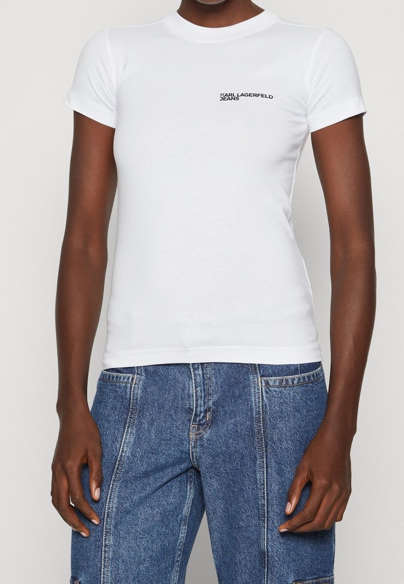 Vit åtsittande t-shirt med korta ärmar och hög halsringning. Har en liten svart logotyptext på bröstet. Slät bomullstextur.