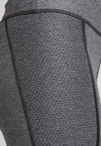 Szare legginsy sportowe z teksturowanym wzorem, płaskimi szwami i kontrastującymi czarnymi panelami bocznymi.
